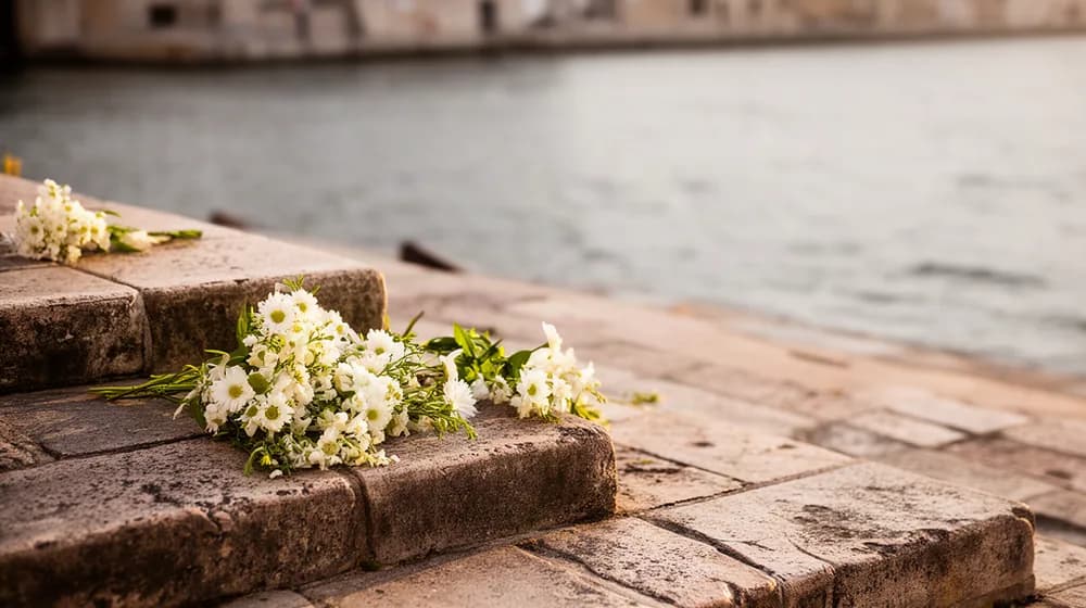 Des marches de pierre usées descendant vers l’eau d’un port, des bouquets déposés sur une marche