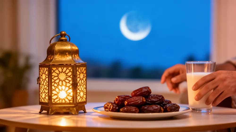 Une lanterne ajourée allumée près d’un plateau de dattes, un croissant de lune derrière la fenêtre