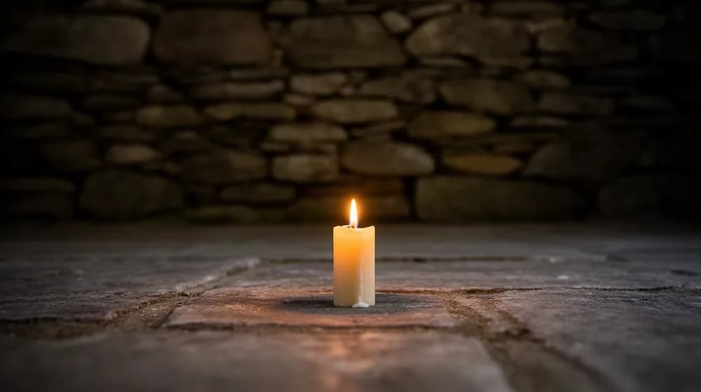 Une unique bougie allumée au ras d’un sol de pierre, le reste dans l’ombre